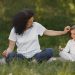 Mother and daughter bonding through yoga outdoors in a serene grassy field.