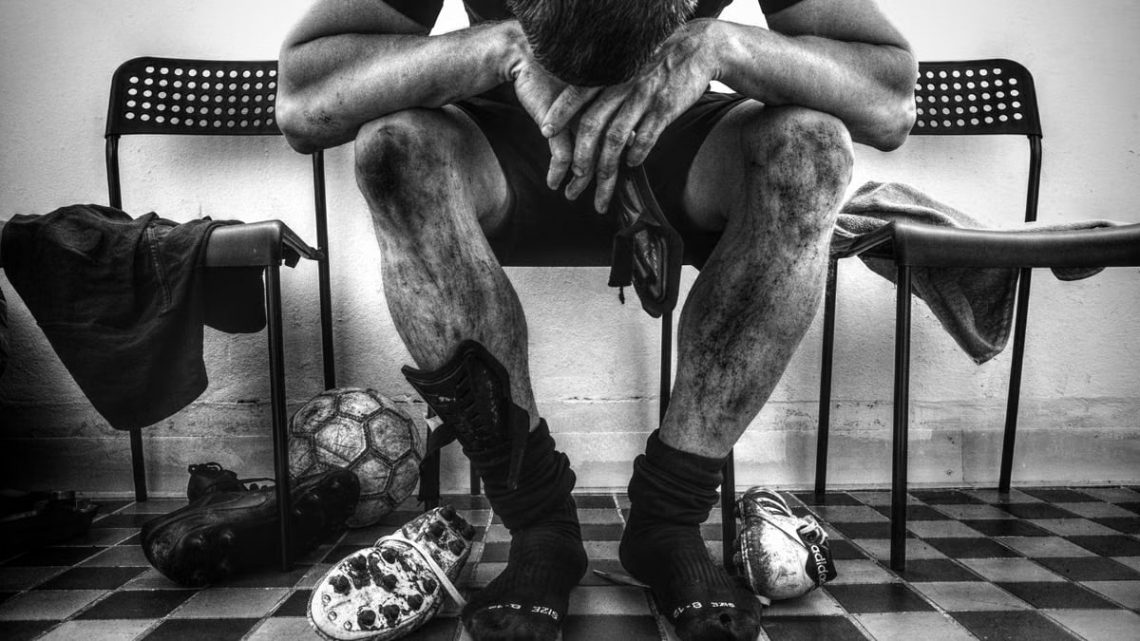 Monochrome image of exhausted soccer player resting in locker room.